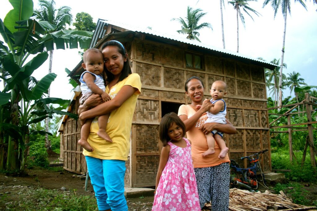 A family smiles in front of their new storm-resistant home built by Medair in the Philippines 