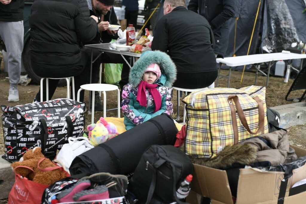 A girl sits amidst bags of belongings.