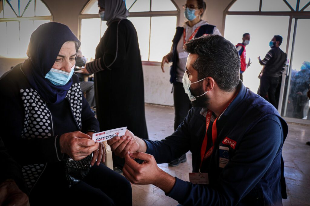 Een Libanese vrouw kijkt naar het vaccinatiebewijs dat ze van een Medair-medewerker krijgt.