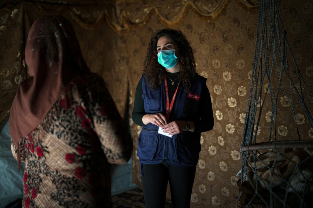 A female primary caregiver talks with a Syrian woman in her tented home.