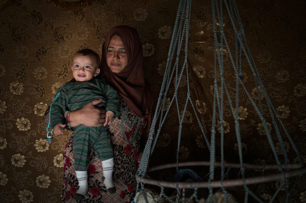 A Syrian mother holds her six-month-old baby boy in their tented home.