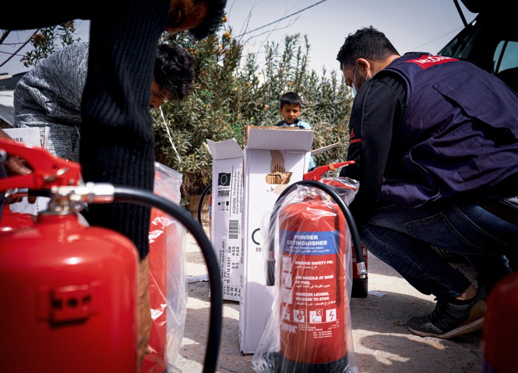 A Medair staff member unboxes a fire extinguisher with other community members.