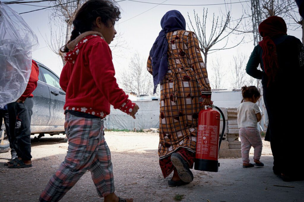 A Syrian community member carries a fire extinguisher, while a girl strolls by.