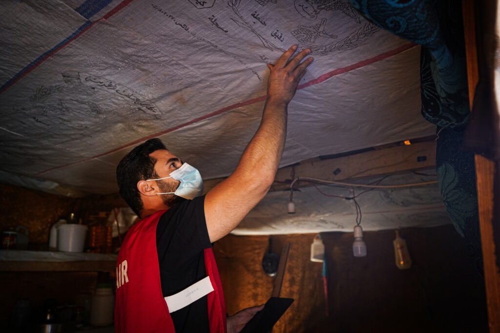 A male volunteer conducting a check up on wooden beams in a tented home.