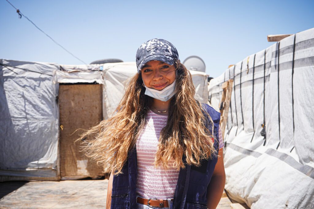 A female volunteer standing in front of a tented settlement