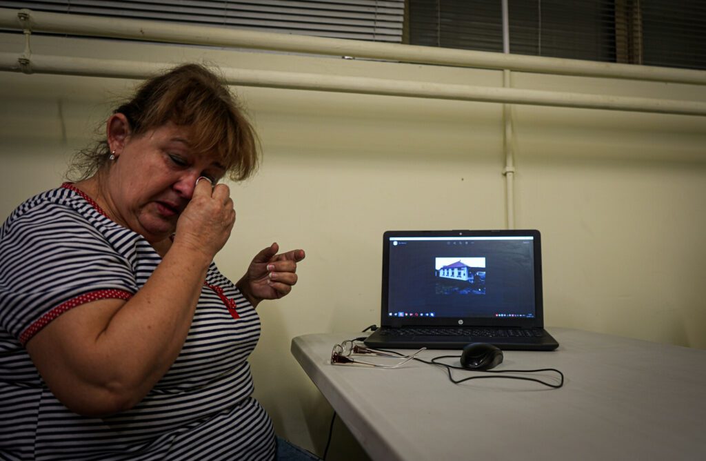 A woman cries in front of laptop displaying a photo of her home.