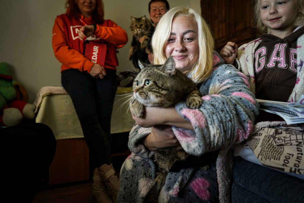 An adult woman holds her cat in a room full of people.