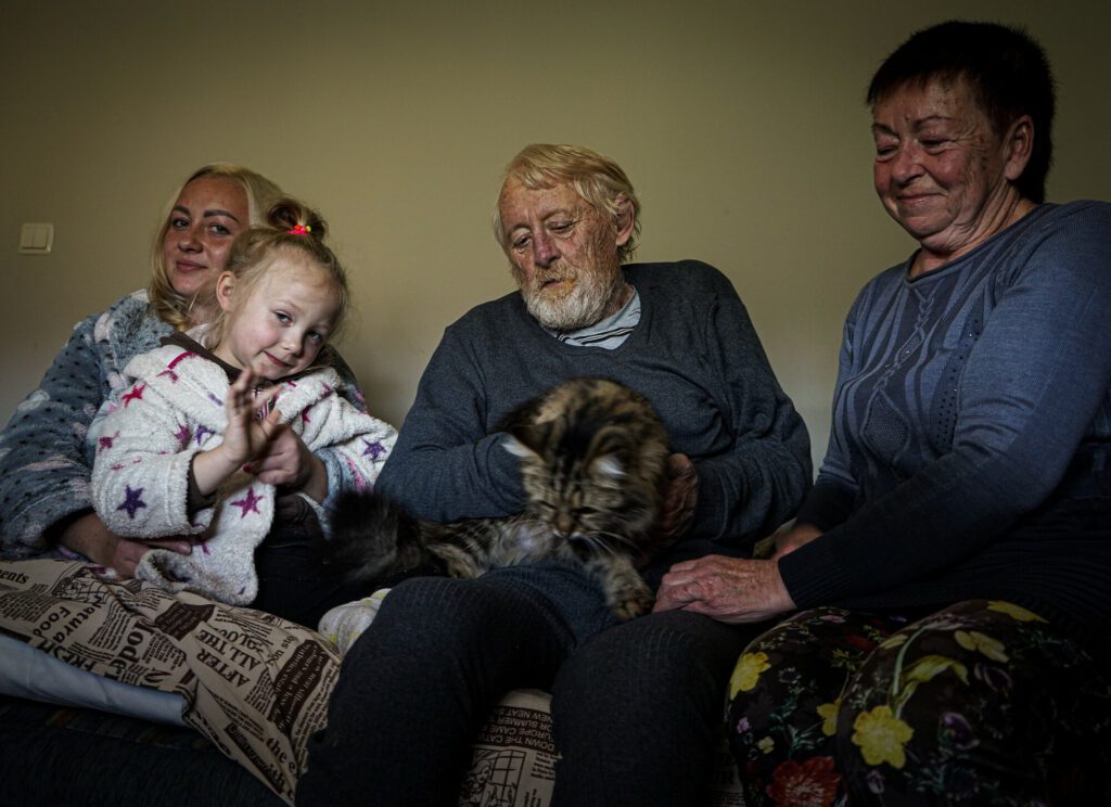 A refugee family from Ukraine sits together in a one bedroom on bed in Poland after fleeing the conflict.