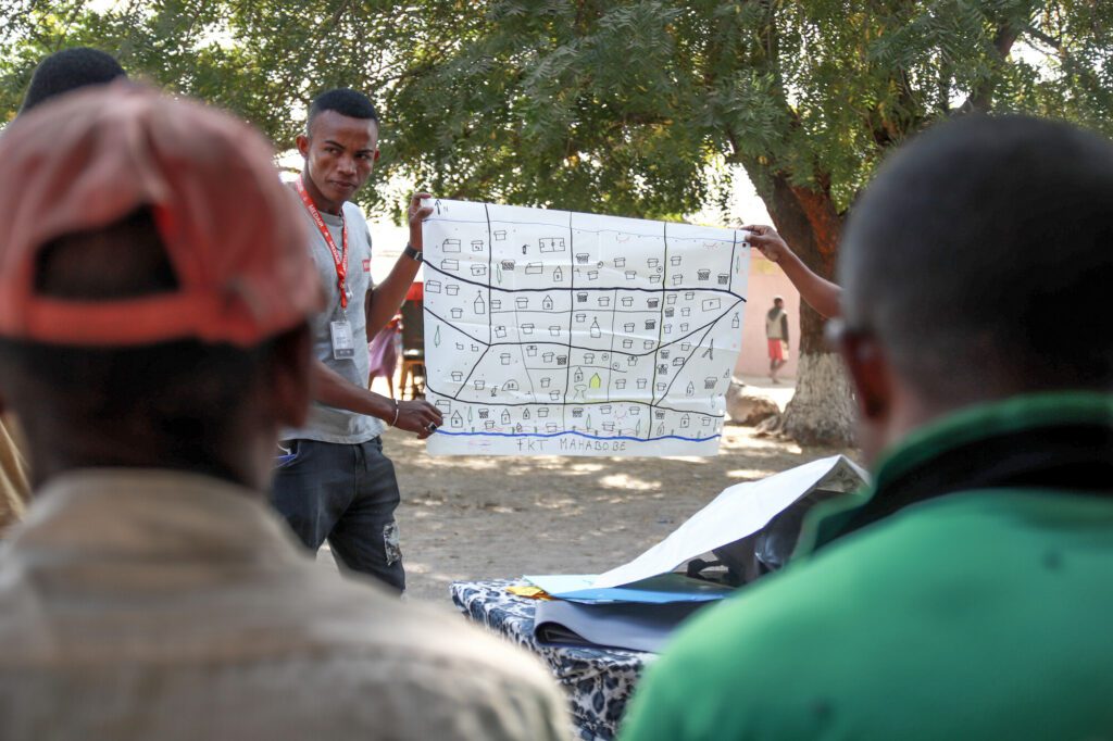  In a village in Madagascar, two men present a hand-drawn map of their community to a small, attentive audience
