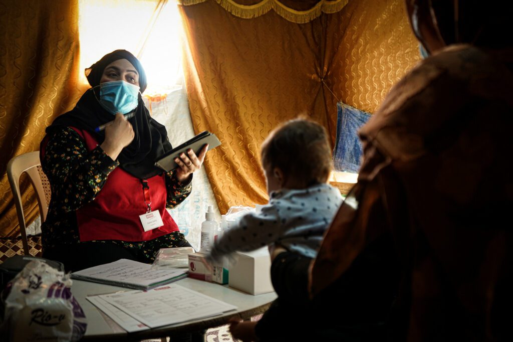 A female primary caregiver during a consultation session with an affected community member in a tented home.
