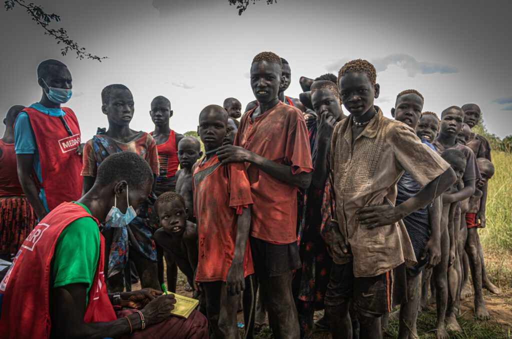 Children in a cattle camp in South Sudan get registered for measles vaccination by a male humanitarian aid worker.