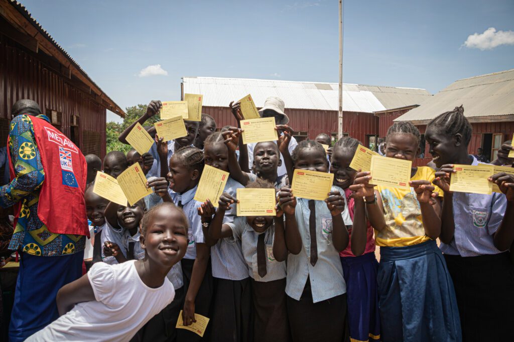 School children on a school yard showing measles vaccination registration cards.