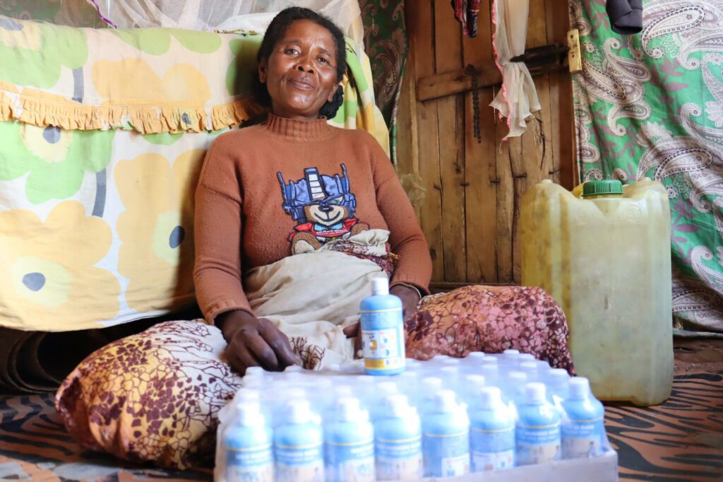 Eine madagassische Frau aus dem Süden des Landes sitzt auf dem Boden ihres Hauses, vor ihr steht eine Packung mit blauen 150ml-Flaschen, die eine Lösung zur Klärung von Wasser enthalten.