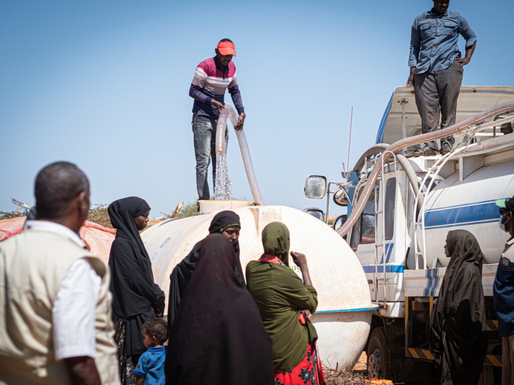 A man directs drinking water with a hose from a truck into a water tank in an IDP settlement in Southern Somalia.