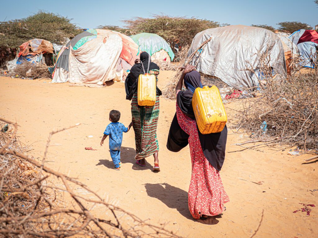Women and a child carrying water on their backs in an IDP settlement in Southern Somalia.
