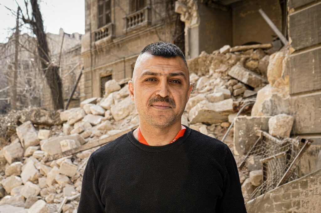 A man stands in front of a collapsed building caused by the devastating Syria - Türkiye earthquakes.