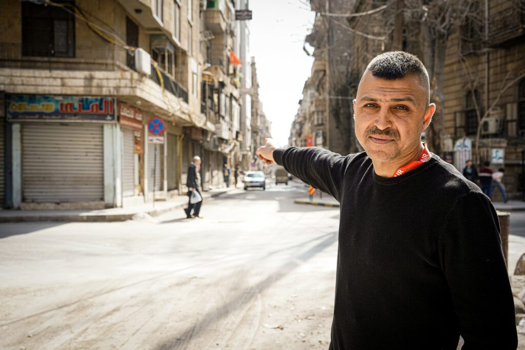 Ein Mann zeigt auf eine Strasse in Aleppo, in der er wohnt. Sie ist von den Zerstörungen durch die Erdbeben in Syrien und der Türkei gezeichnet. 