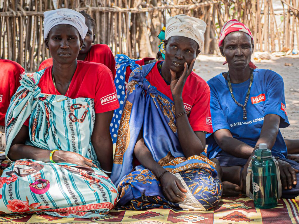 Women in South Sudan sitting on the ground listening to a humanitarian aid worker.