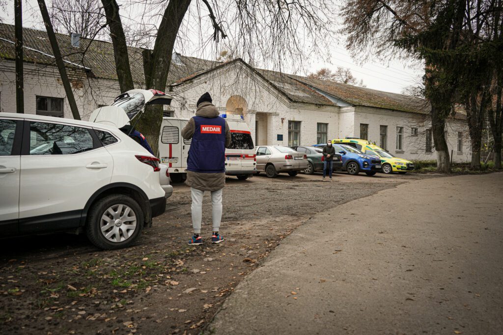 Humanitäre Helfende stehen vor einer Gesundheitseinrichtung in der Ukraine. 