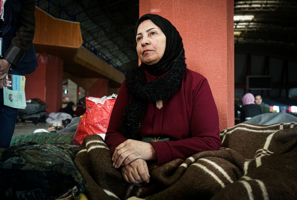 A woman sits on the floor wrapped in a blanket at a sporting stadium in Syria.
