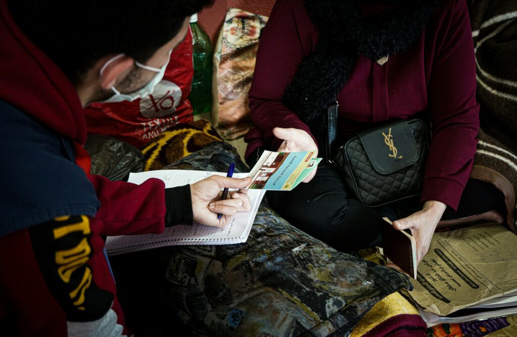 A humanitarian aid worker presents a brochure during a psychological first-aid session with an affected community member.