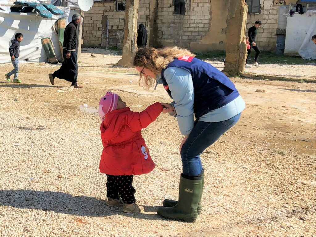 A female humanitarian aid worker greets a little girl at an informal settlement.
