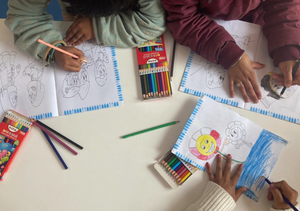 The hands of children holding coloured pencils are seen colouring in pictures of flowers and cartoon characters.