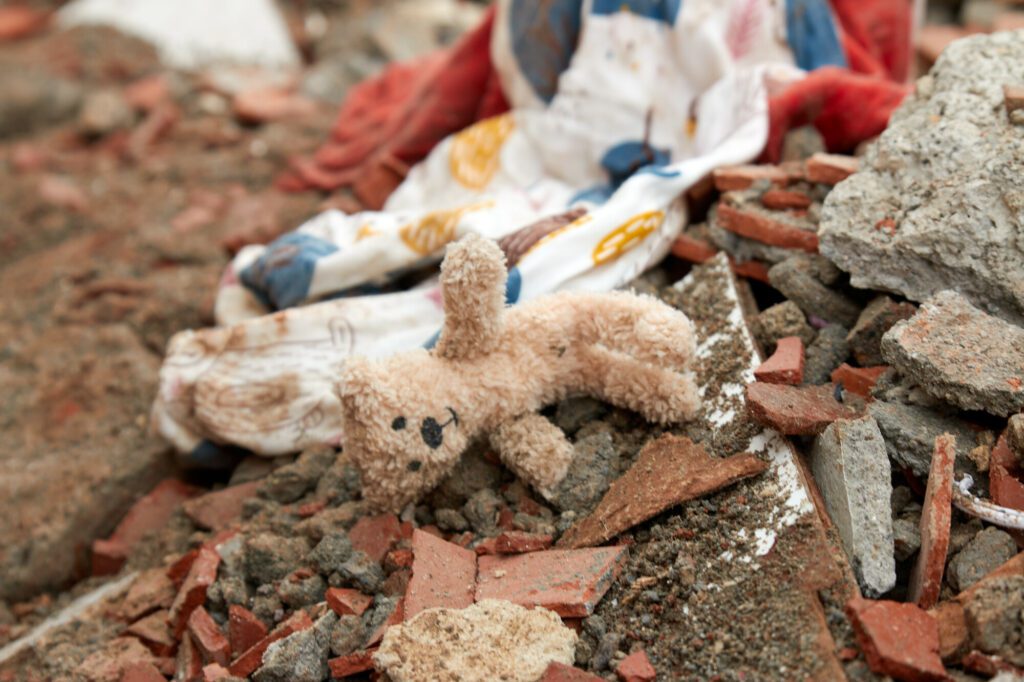 A pink teddy bear lays on its side on a pile of rubble.