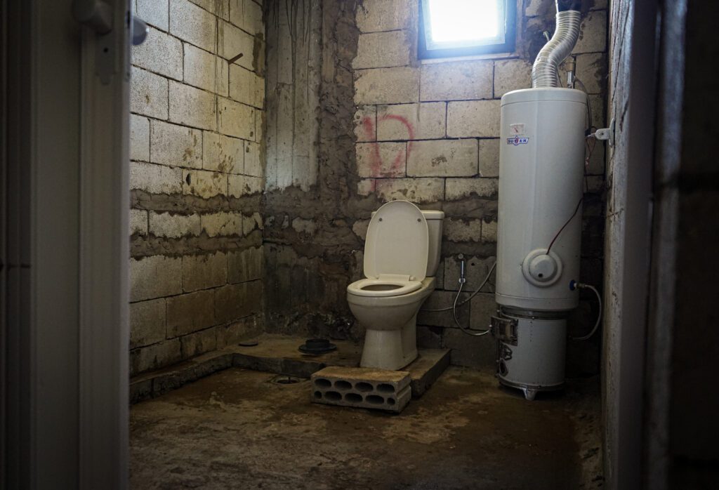 Der Waschraum zeigt einen neu installierten erhöhten Toilettensitz und einen Wasserboiler.