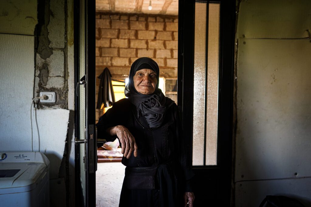 Une femme âgée se tient à l'entrée de sa maison tout en s'appuyant sur une porte en acier fraîchement installée. 