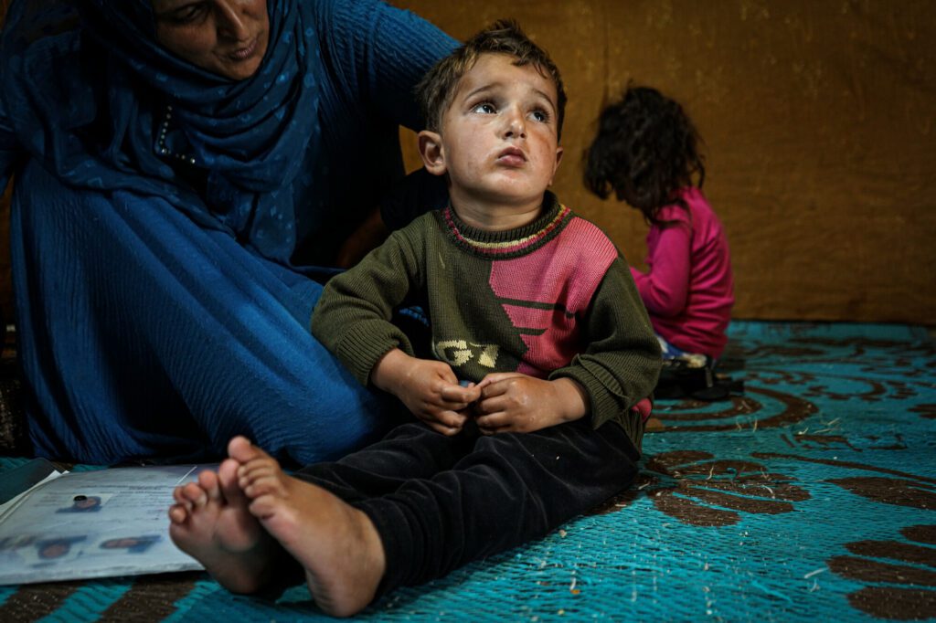 A Syrian community member comforts her baby boy in her tented home.