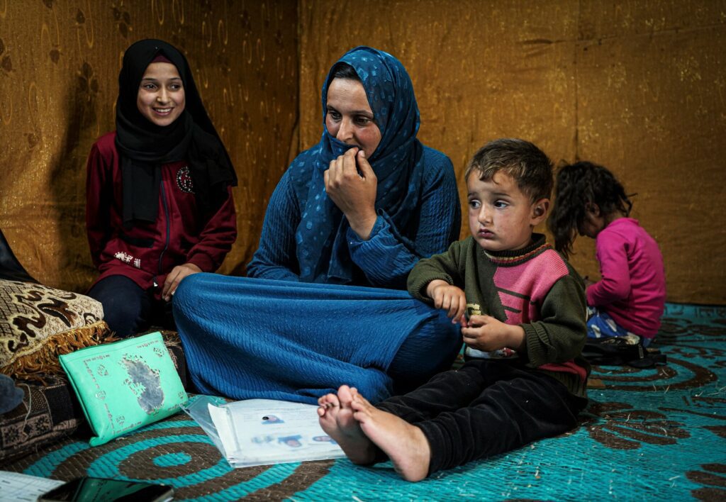 Een Syrische vrouw zit met haar kinderen op de grond in haar tent.