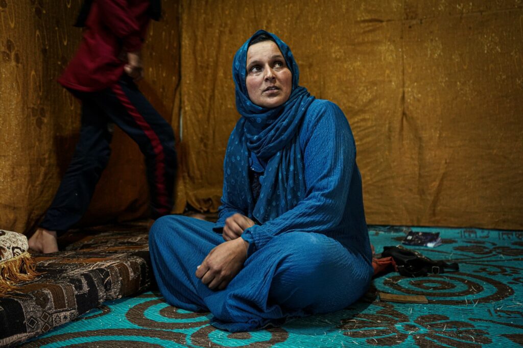 A Syrian community sits on the ground in her tented home.