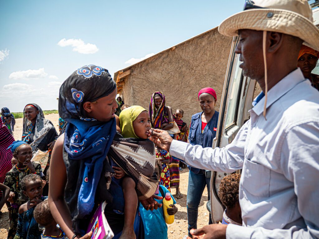 A male humanitarian aid worker immunizes a young girl child of a pastoral nomad community.