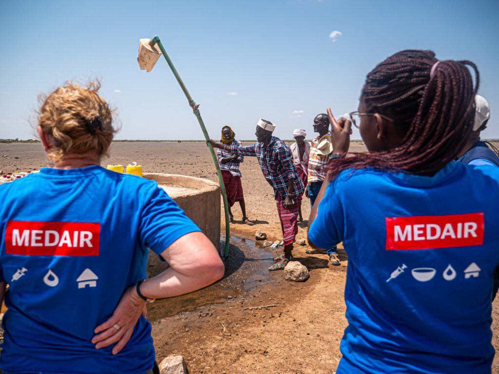 Two female humanitarian aid workers standing at a water point together with local community members in North Horr, Northern Kenya.