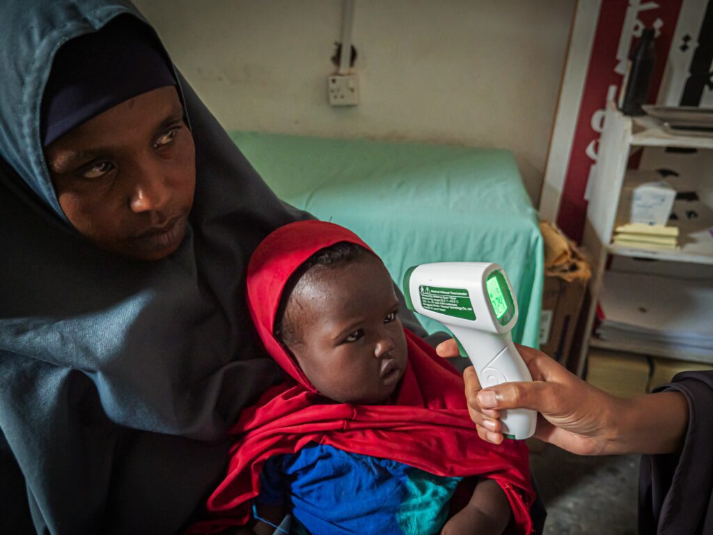 A young girl child's temperature is measured by clinical staff in a health facility in central Somalia.