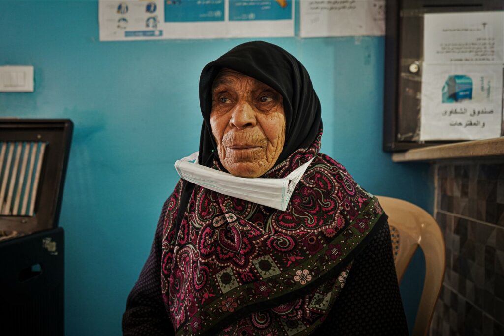 An elderly woman sits at the entrance of a health clinic.
