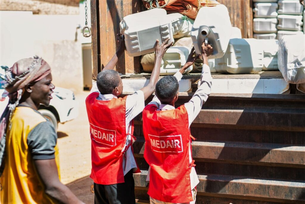 Two male humanitarian aid workers pick water canisters out of a truck in White Nile State, Sudan.